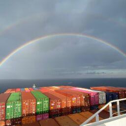 Fracht-Schifffahrt: Containerschiff auf See und Regenbogen