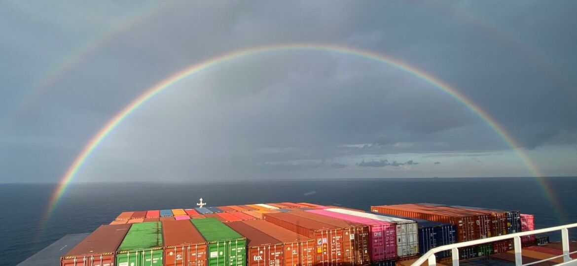 Fracht-Schifffahrt: Containerschiff auf See und Regenbogen