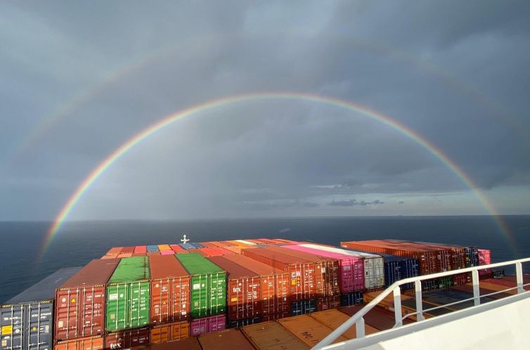Fracht-Schifffahrt: Containerschiff auf See und Regenbogen